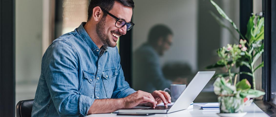 Man sieht einen jungen Mann mit Brille, an seinem Laptop sitzen