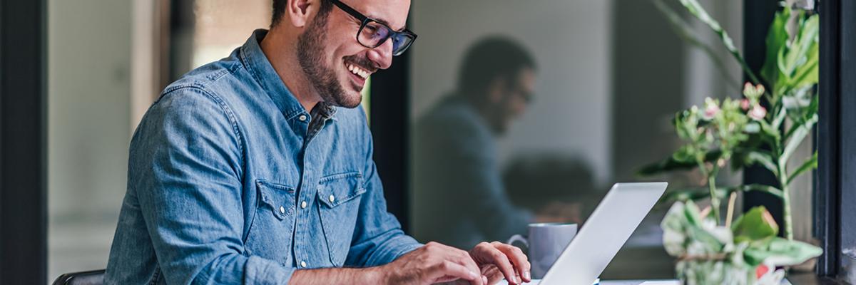 Man sieht einen jungen Mann mit Brille, an seinem Laptop sitzen