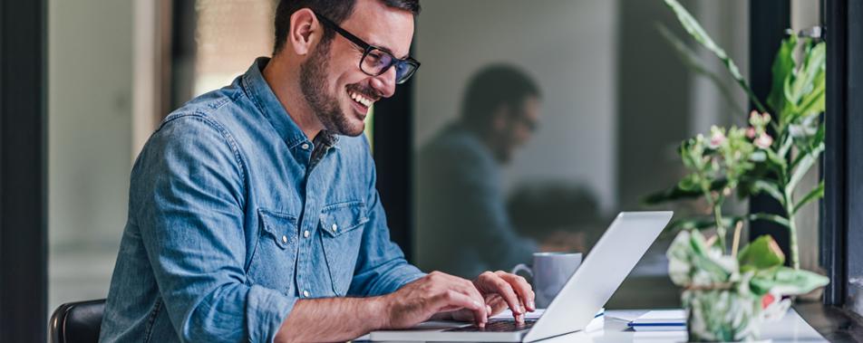Man sieht einen jungen Mann mit Brille, an seinem Laptop sitzen