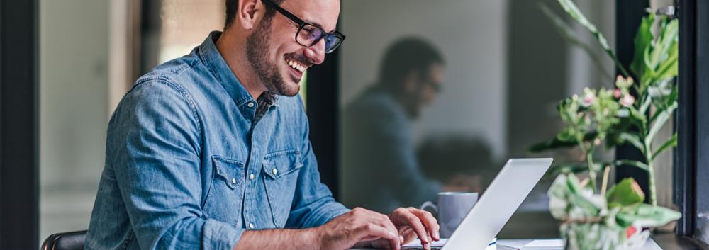 Man sieht einen jungen Mann mit Brille, an seinem Laptop sitzen