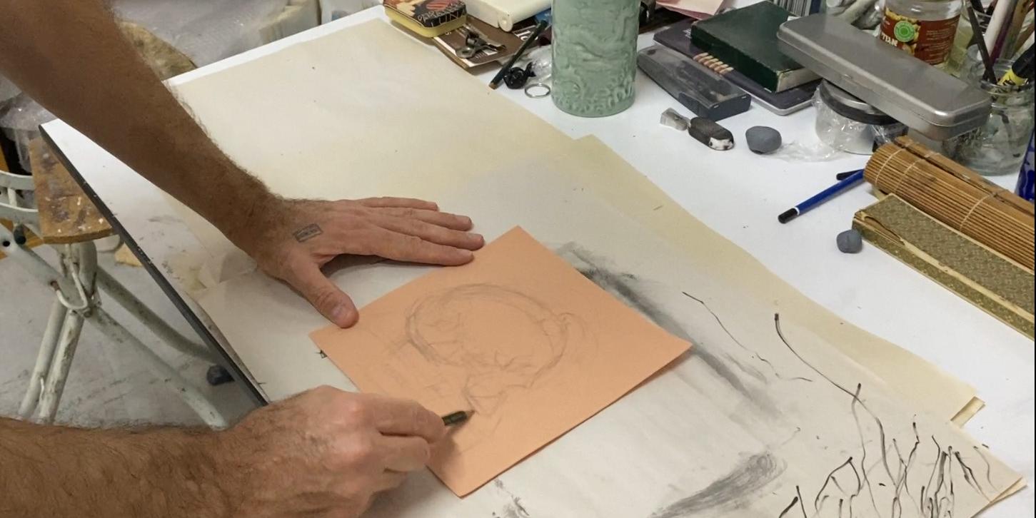 Akademisches Zeichnen - Man sieht zwei Männerhände, die mit einem Kohlestift auf einem Papier zeichnen